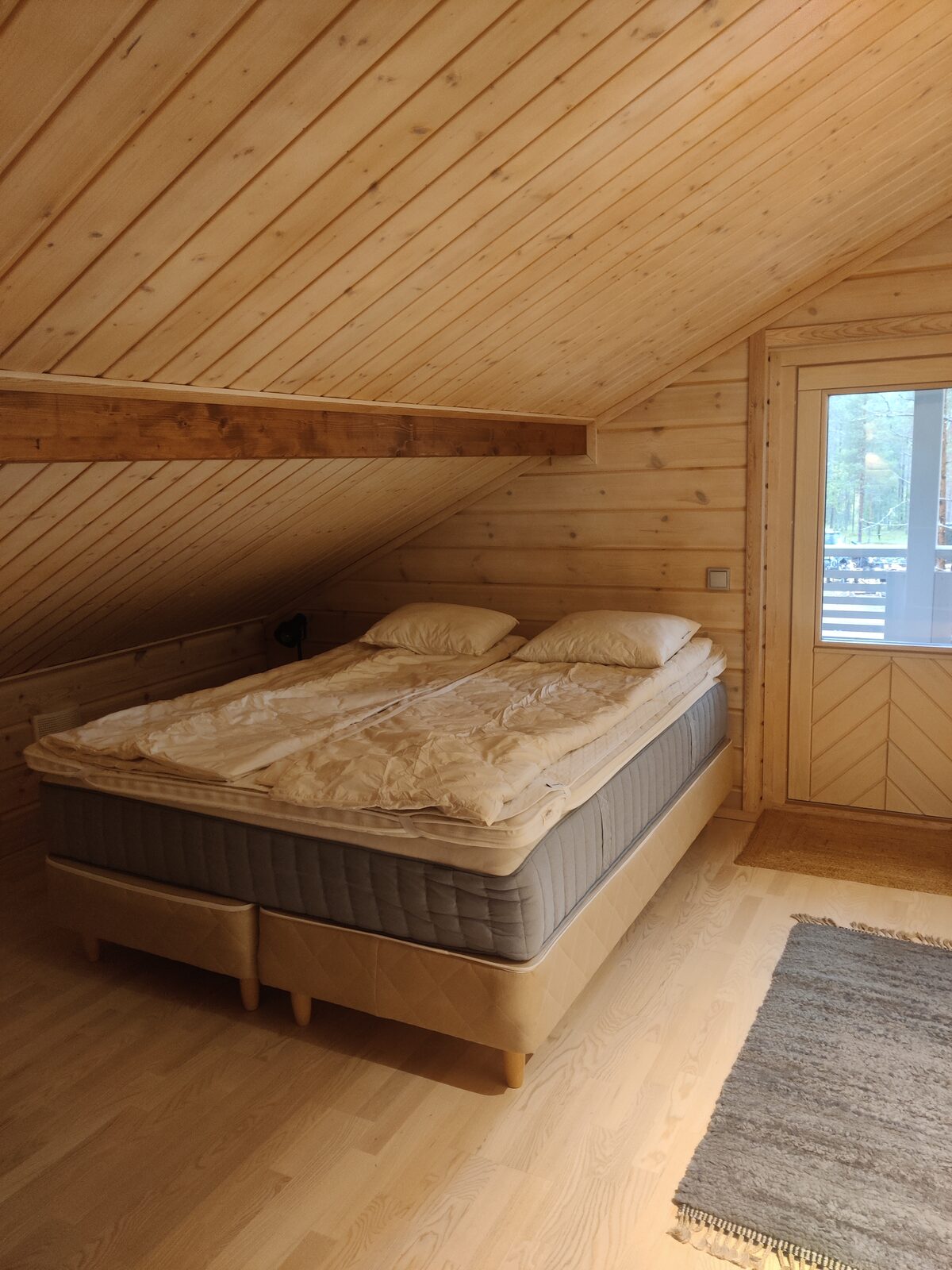 Schlafzimmer unter dem Holzdach mit Doppelbett und Fenster zum Wald